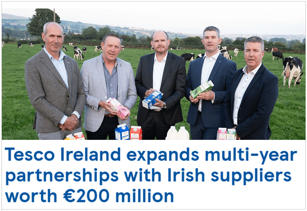 Five businessmen standing in a green field with cows, holding dairy products. Text: "Tesco Ireland expands multi-year partnerships with Irish suppliers worth €200 million"