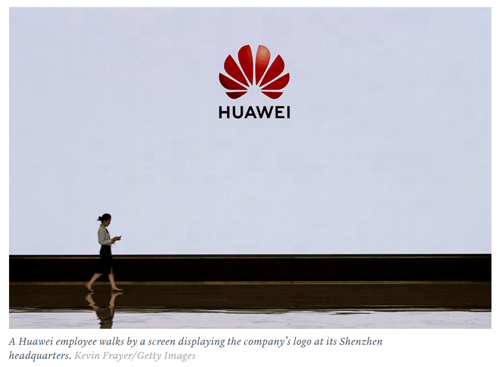 Huawei logo displayed at company headquarters with employee walking past screen